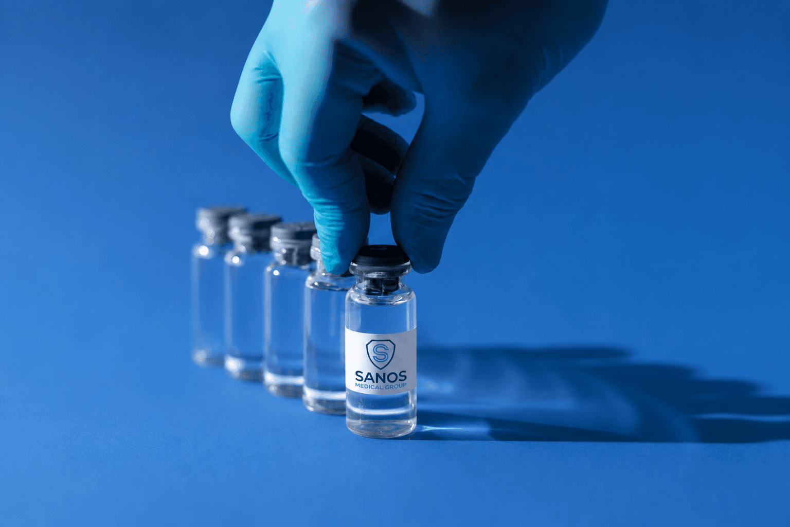 A gloved hand selecting a clinical vial labeled Sanos Medical Group from a row of vials