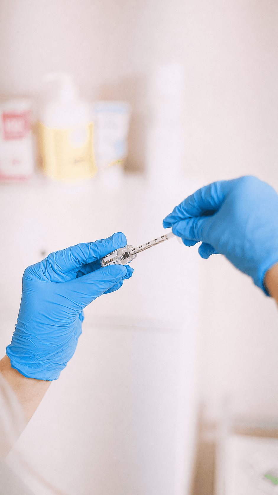 Gloved hands drawing medication from a vial into a syringe in a clinical setting